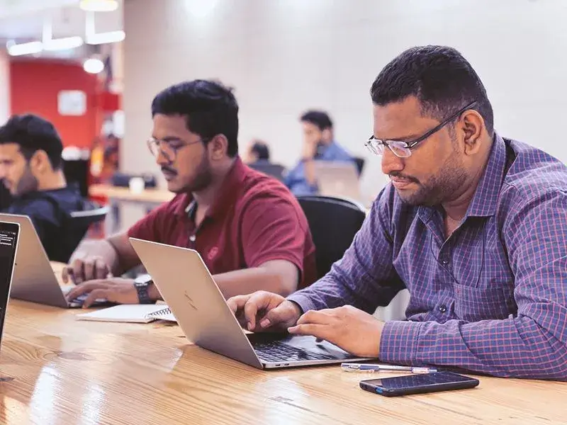 a group of men sitting at a table working on laptops