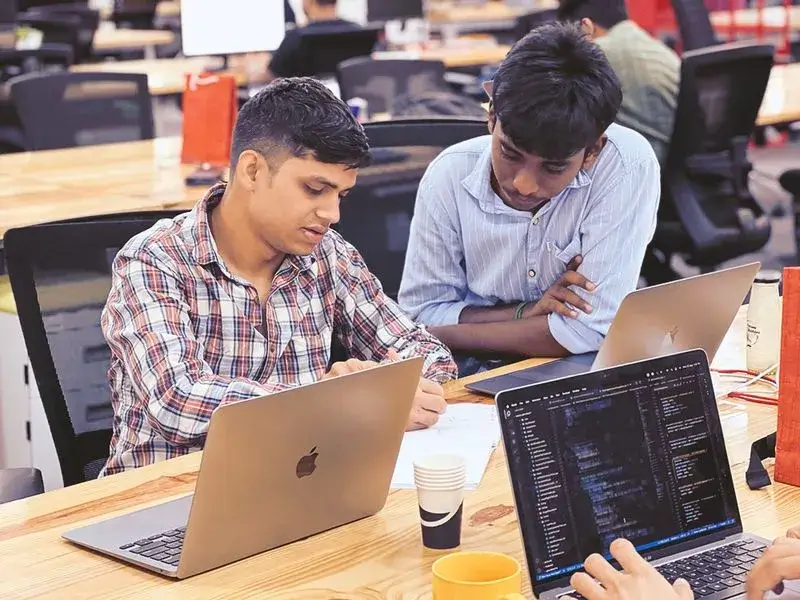 a group of people sitting at a table with laptops